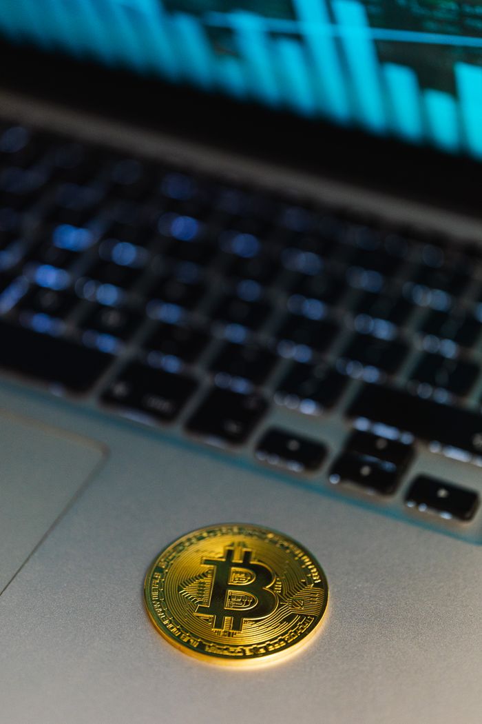 Close-up of a Bitcoin coin on a laptop, with a graph display in the background representing cryptocurrency technology.